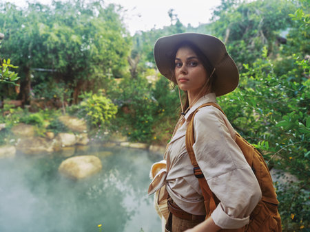 A woman in a hat is standing near a pond with steam coming out of it