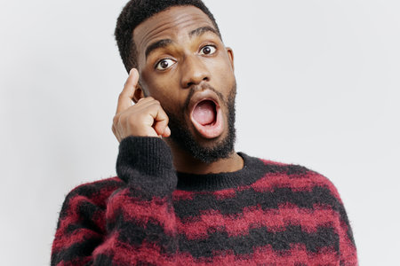 Surprised man in a red and black sweater covering his mouth with hand, expressing shock or disbelief indoorsの写真素材