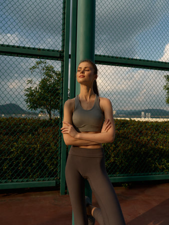 Athletic woman relaxing in a sports environment against a green fence and cloudy sky