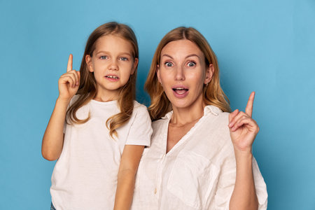 Mother and daughter in playful interaction, pointing fingers at each other on a vibrant blue backgroundの写真素材