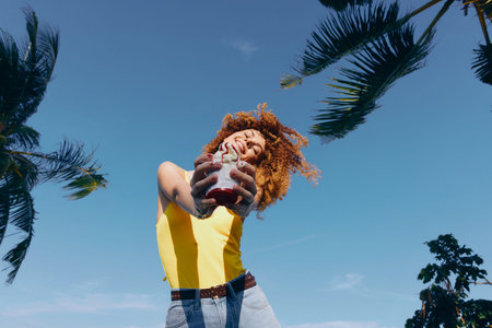 Happy woman enjoying a drink under palm trees against a clear blue sky