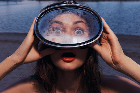 Surprised woman holding a large reflective lens by the water s edge with an open mouthed expressionの写真素材