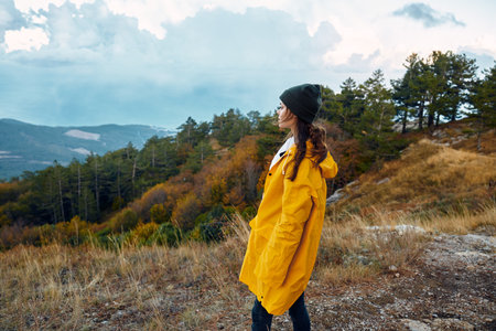 Woman in a yellow raincoat contemplating the majestic mountains while standing on a hilltop in...