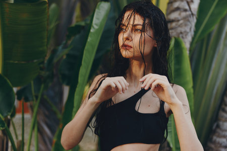 Tropical Escape Woman in Black Bikini Top Standing in Front of Lush Plants and Palm Treesの写真素材