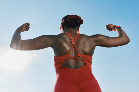 Strong athlete woman flexing muscles outdoors against a bright skyの写真素材