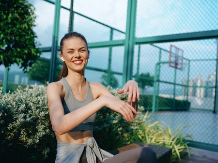 Young woman exercising outdoors with a joyful smile in a sports outfit against a sunny urban backdropの写真素材