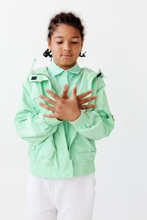Young boy wearing a green jacket and white pants poses with hands on chest in trendy fashion pose