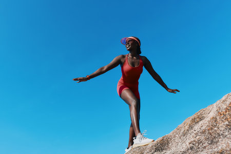 Young woman in a red swimsuit joyfully balancing on a rock against a clear blue skyの写真素材