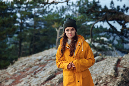 A young woman wearing a yellow raincoat standing on a rocky hill with trees in the background during a nature tripの写真素材