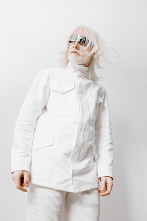 Fashionable model wearing a modern white outfit with unique sunglasses, standing against a minimalist light background, showcasing contemporary style and innovation in fashion photographyの写真素材