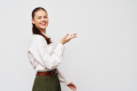 Smiling woman in a white shirt and green pants on a neutral background, showcasing warmth and friendliness in a professional setting, exuding confidence and approachabilityの写真素材
