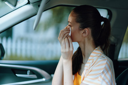 Emotional young woman sitting in a car wiping tears, wearing a yellow top and striped cover, captured on a softly blurred background Image conveys feelings of sadness and reflectionの写真素材