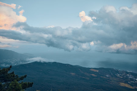 A stunning view of the vast ocean from the majestic peak of a mountain with fluffy clouds in the skyの写真素材