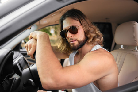 A muscular man with long hair wearing sunglasses inside a car, exuding a confident attitudeの写真素材