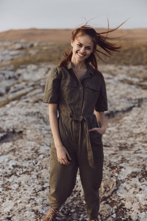 Woman standing on rocky hill in olive green jumpsuit with hair blowing travel beauty fashion art conceptの写真素材