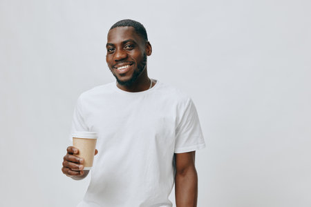 Smiling man holding a coffee cup, wearing a white t shirt, on a light background with a joyful expression, showcasing confidence and casual style Perfect for lifestyle and positivity themesの写真素材