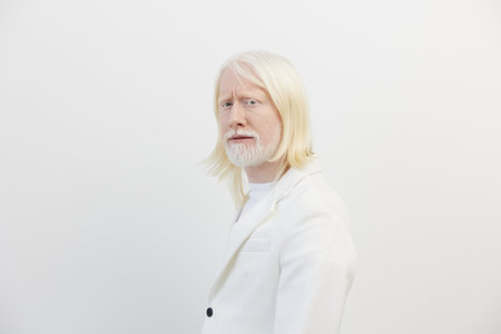Portrait of an older man with long white hair and beard, wearing a stylish white suit, against a soft white background, exuding confidence and wisdomの写真素材