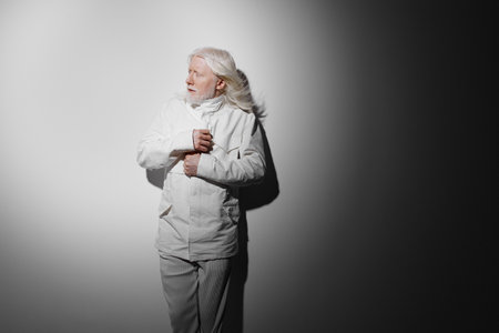 elderly person in white clothing, light and shadow contrast, thoughtful expression, in a minimalist setting, highlighting emotions of introspection and calmness with a sleek backgroundの写真素材