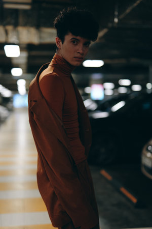 Portrait of a young person in a stylish brown outfit standing in a dimly lit parking garageの写真素材