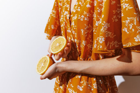 Woman in orange dress holding lemon slices against white wallの写真素材