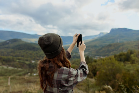 A woman captures a stunning mountain landscape on her cell phone during a travel adventureの写真素材