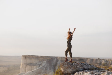 Woman standing proudly atop mountain peak with arms raised in joyful triumph in nature beauty concept of achievement and adventure in travel and successの写真素材
