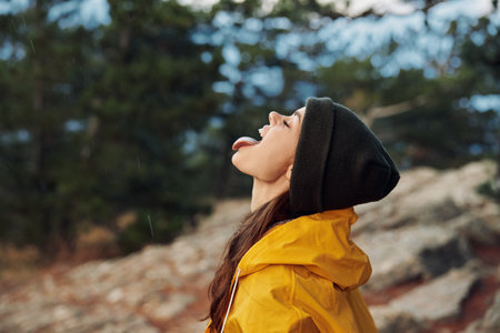 A stylish woman in a bright yellow raincoat and hat enjoying the rain with her mouth open in awe of the beauty of natureの写真素材