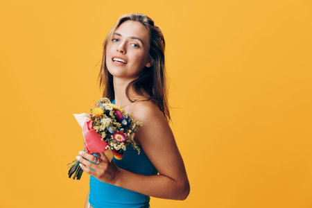 Gorgeous woman holding vibrant bouquet of flowers in front of sunny yellow backdrop stock imageの写真素材
