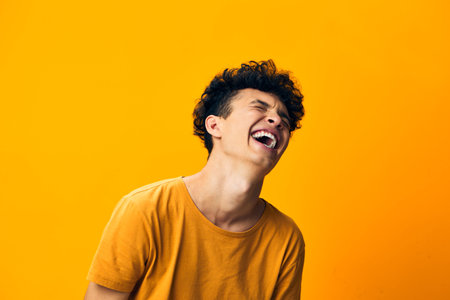 joyful young man laughing against a vibrant orange background, showcasing carefree happiness and positivity, perfect for conveying emotions and cheerful moments in photographyの写真素材