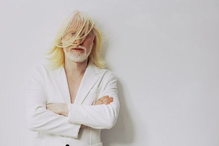Elegant man with long white hair dressed in a stylish white suit, standing confidently against a soft white background, embodying sophistication and charismaの写真素材