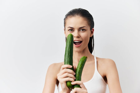 woman holding cucumbers, healthy lifestyle, wellness concept, bright background, fun expression, fresh vegetables, natural beauty, playful gesture, nutrition focus, simple aestheticsの写真素材