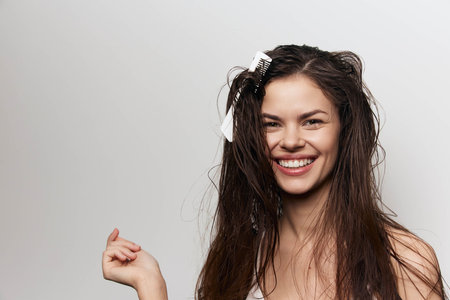 Smiling woman with wet hair and hair clips in a close up portrait against a light gray background, showcasing a cheerful and carefree mood Natural beauty and youthful energy are highlightedの写真素材