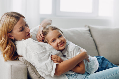 Mother and daughter sharing a tender moment on a cozy couch against a minimalist white backdropの写真素材