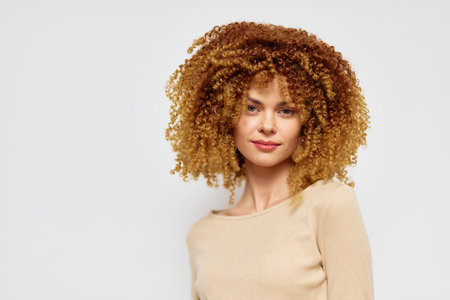 Woman with curly hair in a beige top against a light background showcasing natural beauty and confidence Her vibrant curls contrast beautifully with the neutral tonesの写真素材