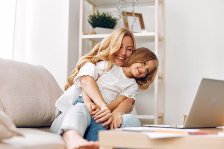 Mother and child bonding on a cozy couch, sharing a moment of learning and fun with a laptopの写真素材