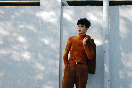 Stylish young man in brown turtleneck against a textured white wallの写真素材