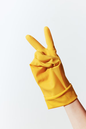 Person in yellow rubber glove making peace sign on white backgroundの写真素材