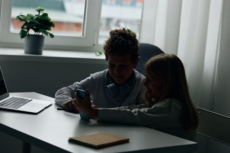 Caucasian children studying at home using laptops and headphones. They are sitting at a table in the living room, fully immersed in their online education. The siblings are engaged.の写真素材