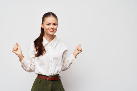 Smiling young woman with long hair in a white shirt and green pants, posing cheerfully against a plain white background, conveying a sense of happiness and positivityの写真素材