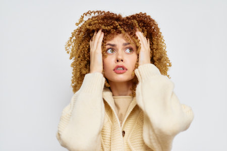 anxious woman with curly hair looking up, wearing a cozy sweater against a light background, expressing concern and contemplation in a close up shotの写真素材