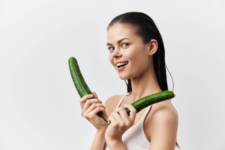 Fresh cucumbers, healthy lifestyle, beauty concept with model smiling holding cucumbers in studio shot, natural elements, white background, vibrant colors highlighting freshness and wellnessの写真素材