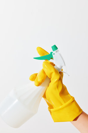 Woman in yellow rubber gloves holding a spray bottle on white backgroundの写真素材