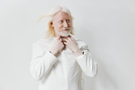 Portrait of a smiling older man in a white suit, set against a soft white background, conveying positivity and serenity His light hair and beard create a warm ambiance in the imageの写真素材