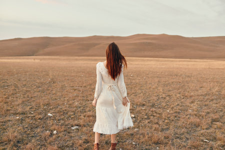 A woman in a white dress standing in the middle of an open field with mountains in the backgroundの写真素材