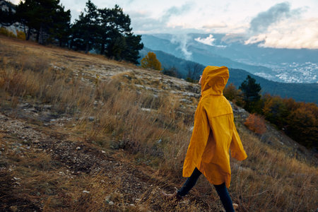 Hiker in Yellow Raincoat Walking on Trail in Woods with Mountain View and Travel Adventure Beauty in Nature Landscape Backgroundの写真素材