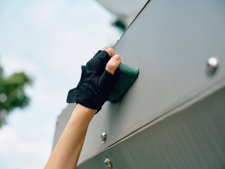 Hand in a black glove cleaning a smooth gray surface outdoors with a blurred green backgroundの写真素材