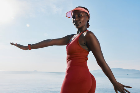 Young woman in a red athletic outfit posing by the seaside during sunrise, showcasing confidence and fitnessの写真素材