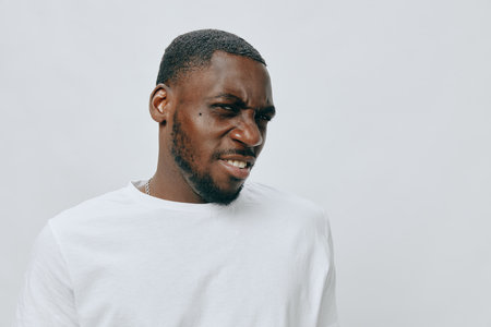 Portrait of an African male model with a serious expression, wearing a plain white t shirt against a light gray background, showcasing emotions and modern fashion stylesの写真素材
