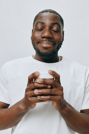 Smiling man holding a cup in a white t shirt, expressing joy and satisfaction. Neutral background highlights the subject's emotions and happiness. Close up portrait with soft lighting.の写真素材