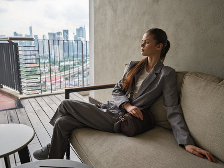 Woman in a gray suit sitting on a balcony overlooking a city skylineの写真素材